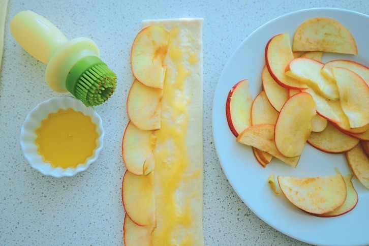 Смажь полоску жидким медом. На край теста выложи ломтики яблока по всей длине. На этом этапе можно добавить корицу.