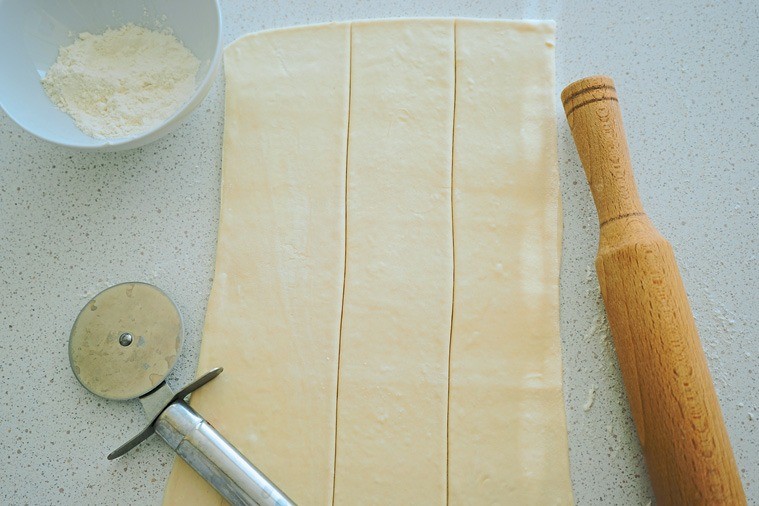 Присыпь стол небольшим количеством муки и раскатай тесто в пласт толщиной 5 мм. Разрежь пласт на полоски шириной примерно в 5 см. 