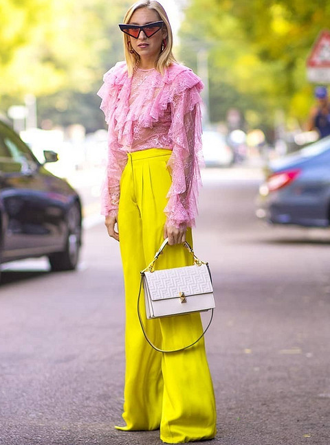 Воздушная нежно-розовая блуза с рюшами и желтые неоновые брюки палаццо — удачный пример контрастного сочетания цветов из разных опер. Здесь даже не потребуются аксессуары, а сумка подойде...