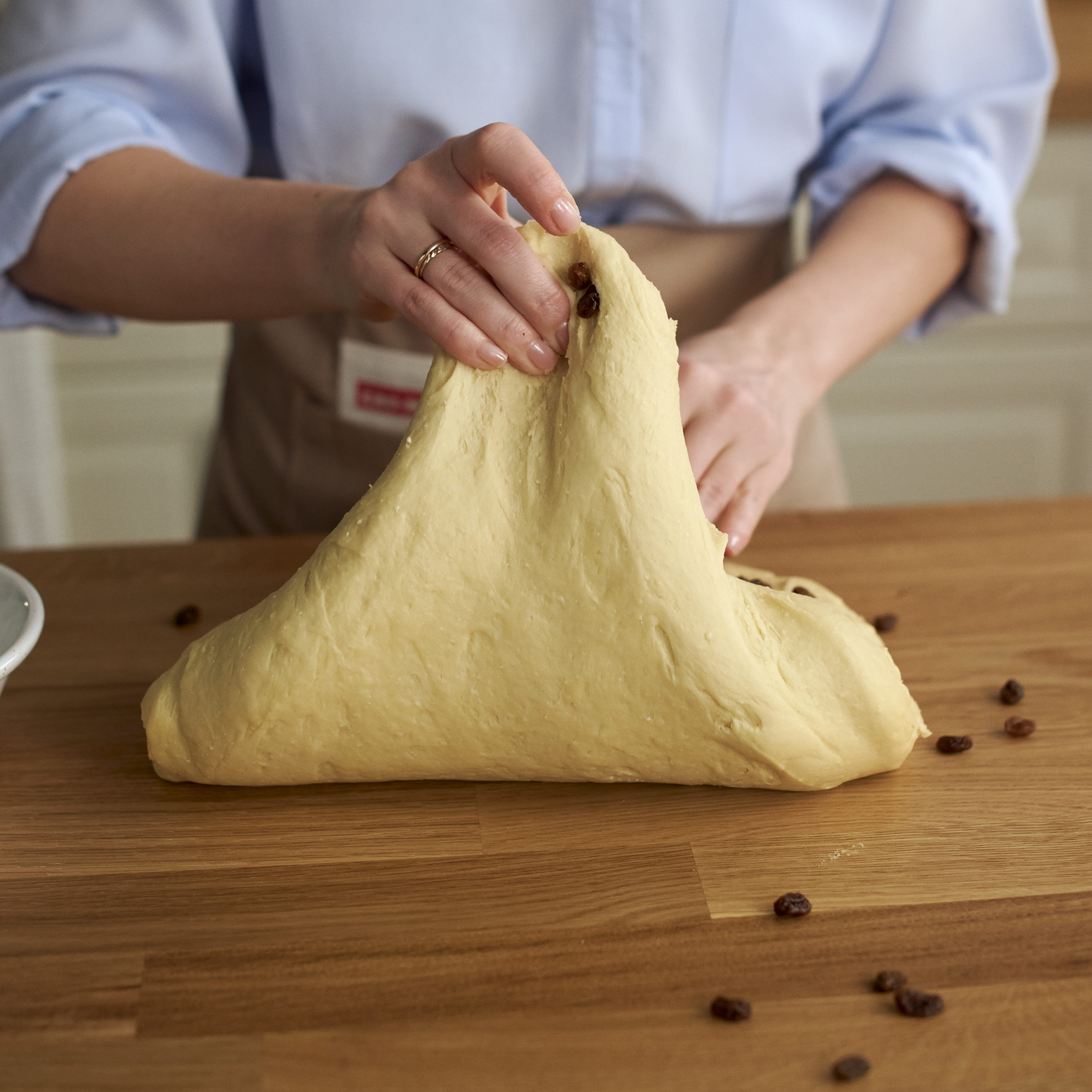 Подпыли стол мукой, переложи тесто из емкости на стол и постепенно вмешивай предварительно обсушенный изюм.
Вымешивай тесто до равномерного распределения изюма по всему объему. После этог...