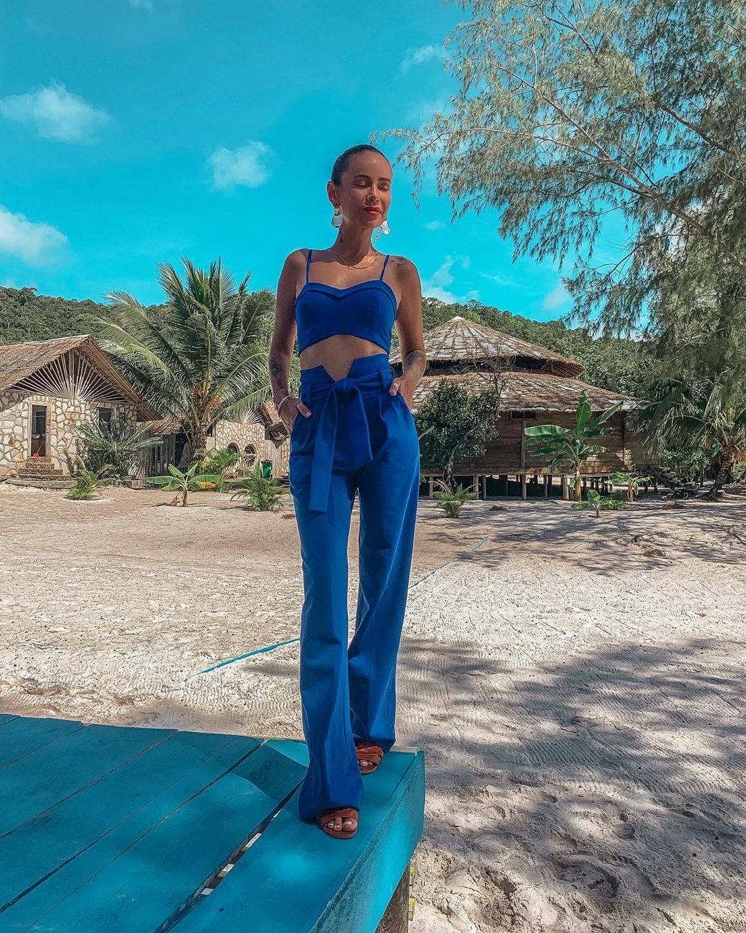 Айза Анохина проводит отпуск в костюме из укороченного топа и расклешенных брюк насыщенного синего цвета с минимумом макияжа и украшений.